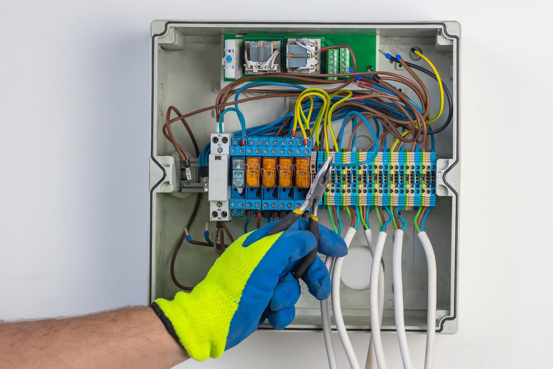 Gloved hand wiring an electrical control panel with colorful cables and terminal blocks