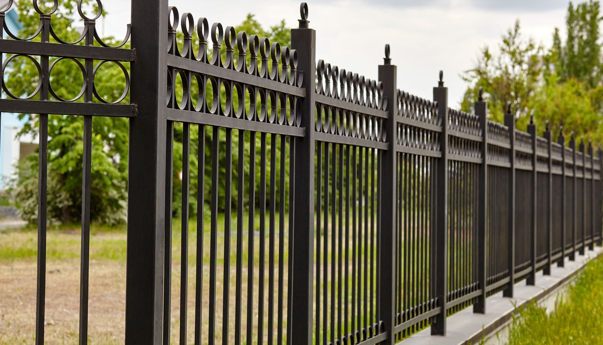 A black wrought iron fence surrounds a grassy field.