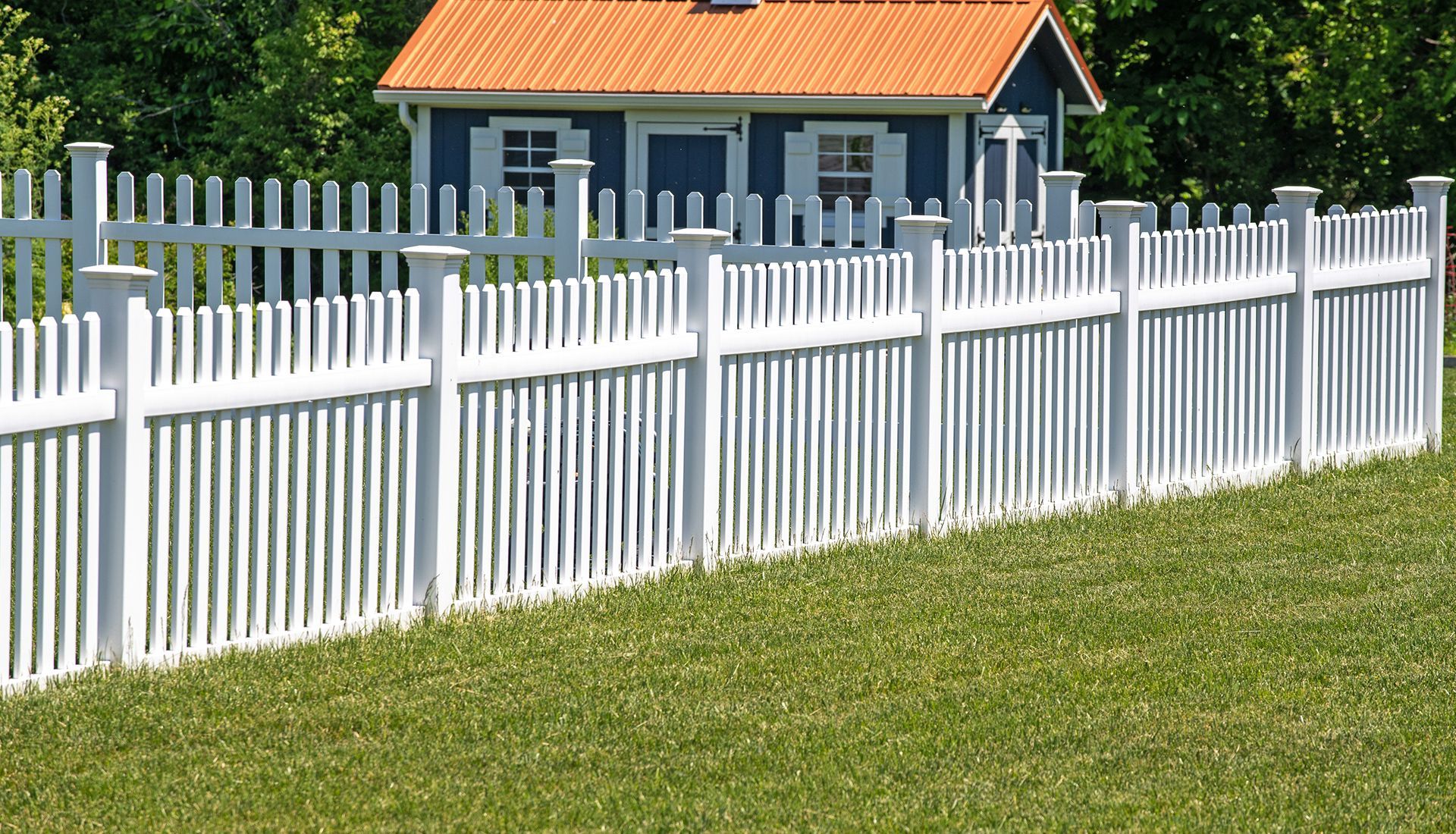 A white picket fence surrounds a small house with an orange roof.