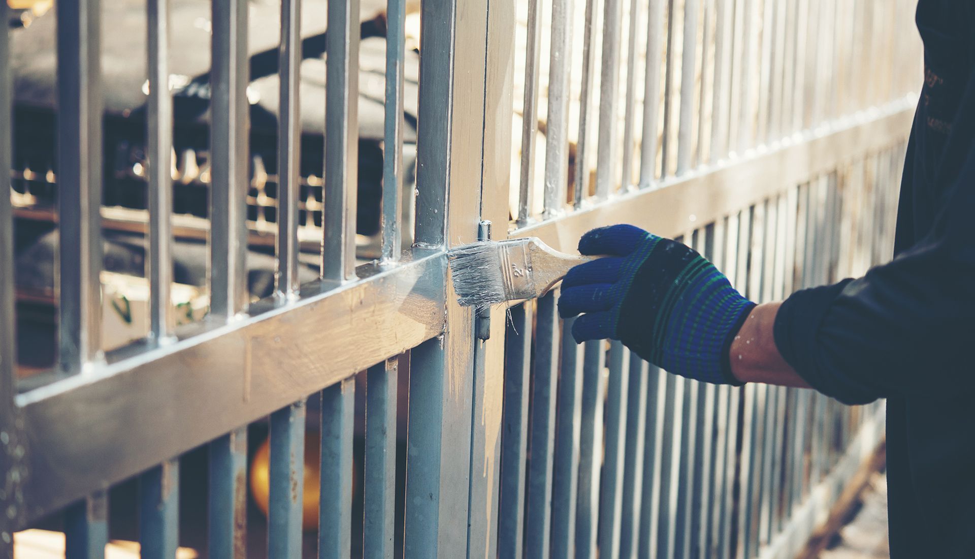 A person is painting a metal fence with a brush.
