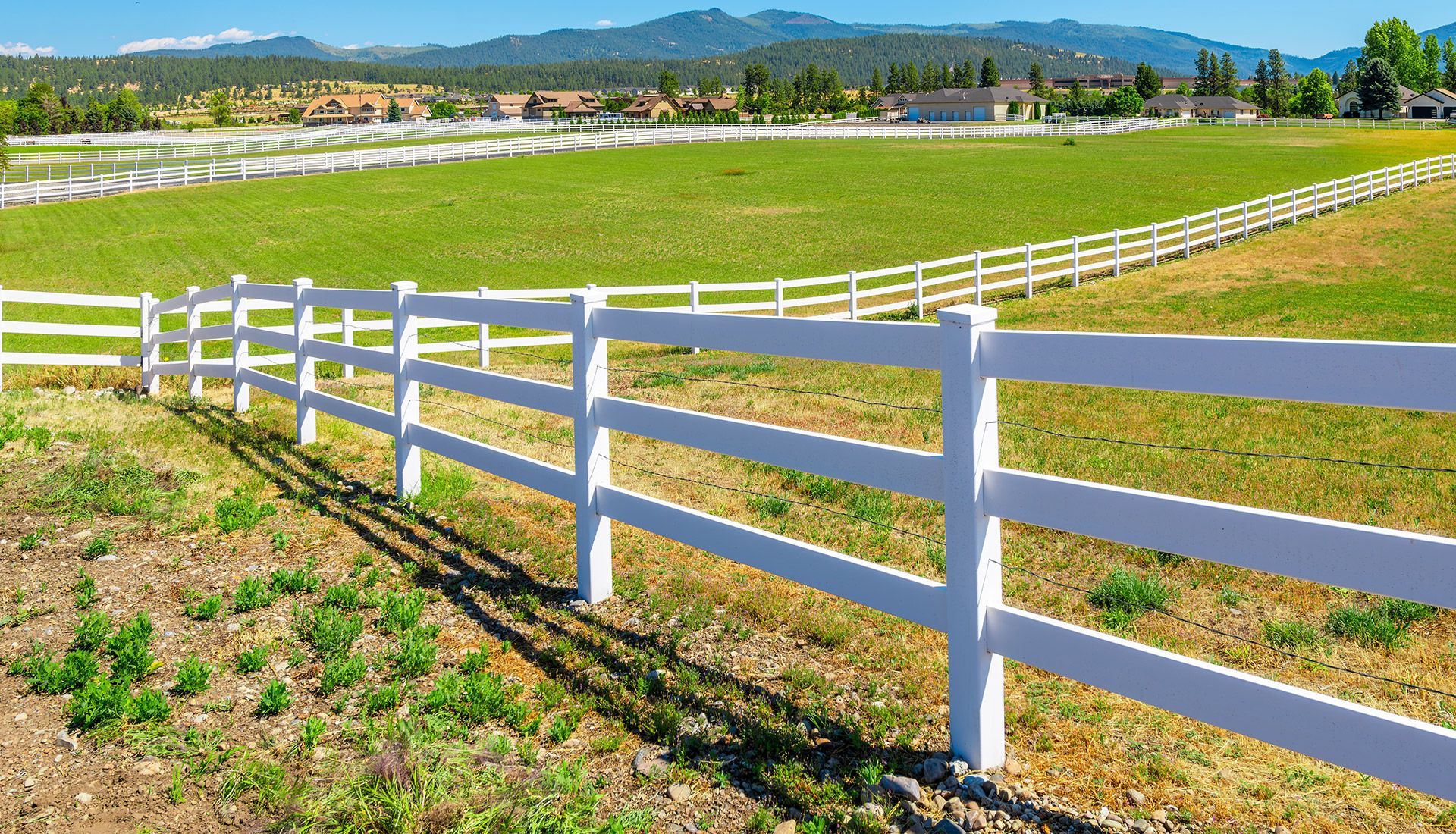 A white fence surrounds a grassy field with mountains in the background.