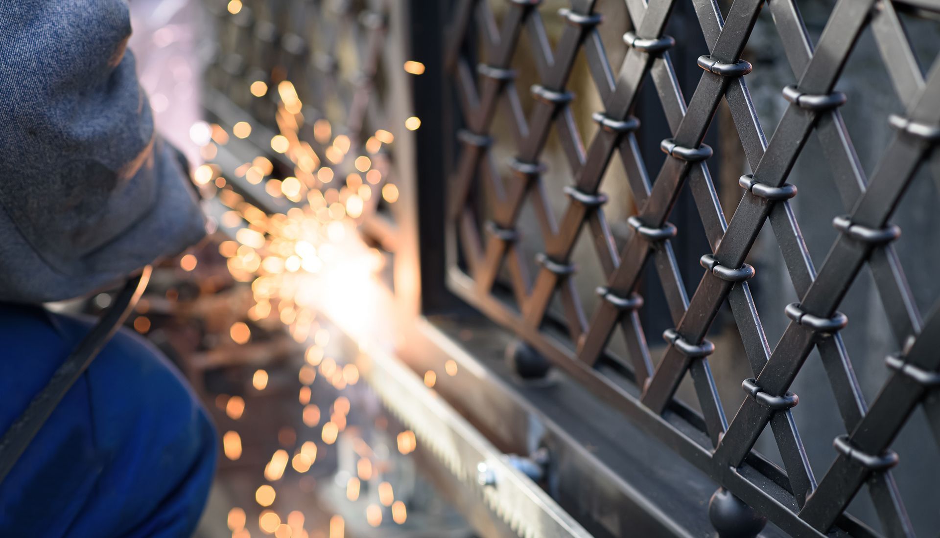 A man is welding a metal fence with sparks coming out of it.