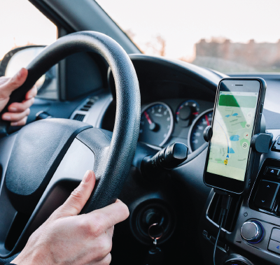 Person driving car, hands on steering wheel, phone with map mounted on dashboard.