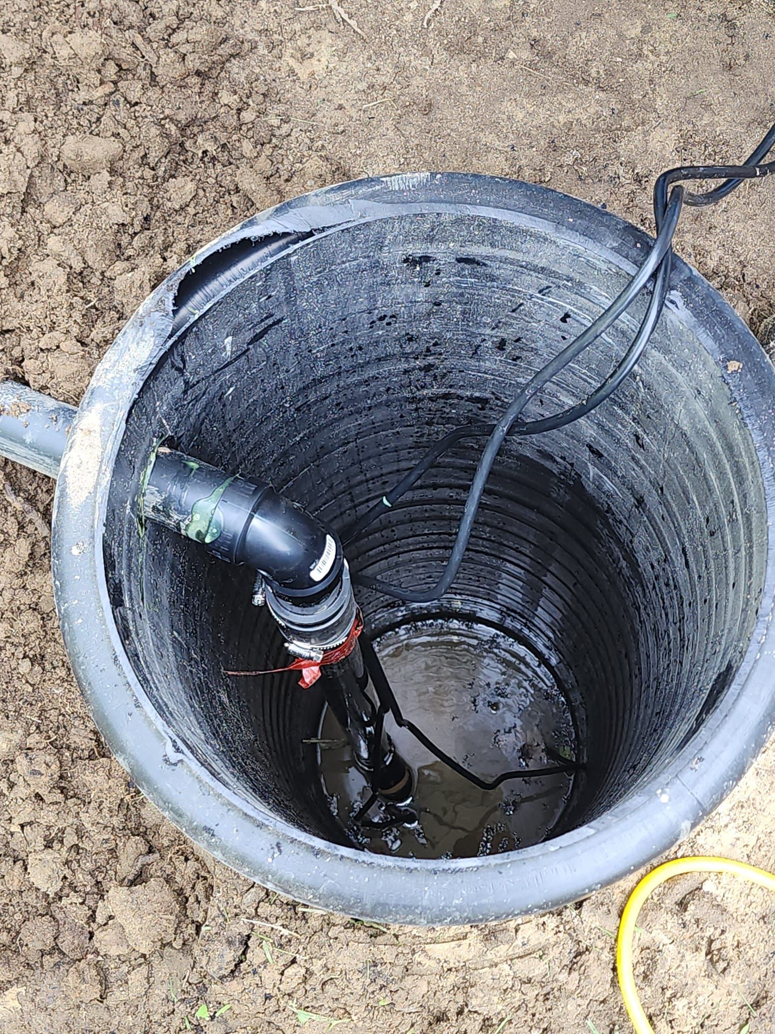 A black bucket with a hose attached to it is sitting in the dirt.