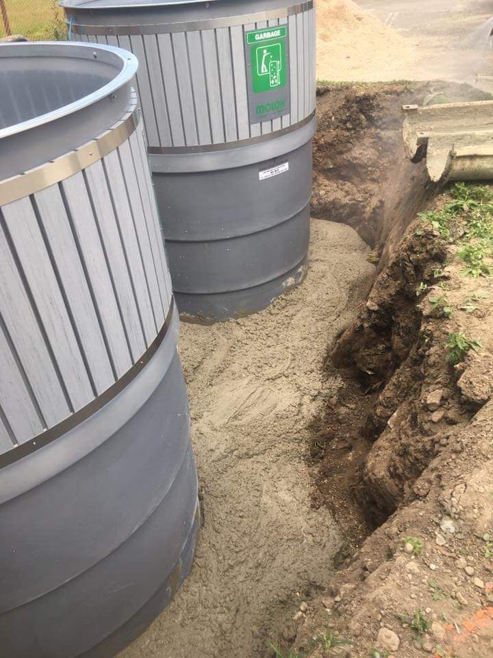 Two trash cans are sitting next to each other in the dirt.