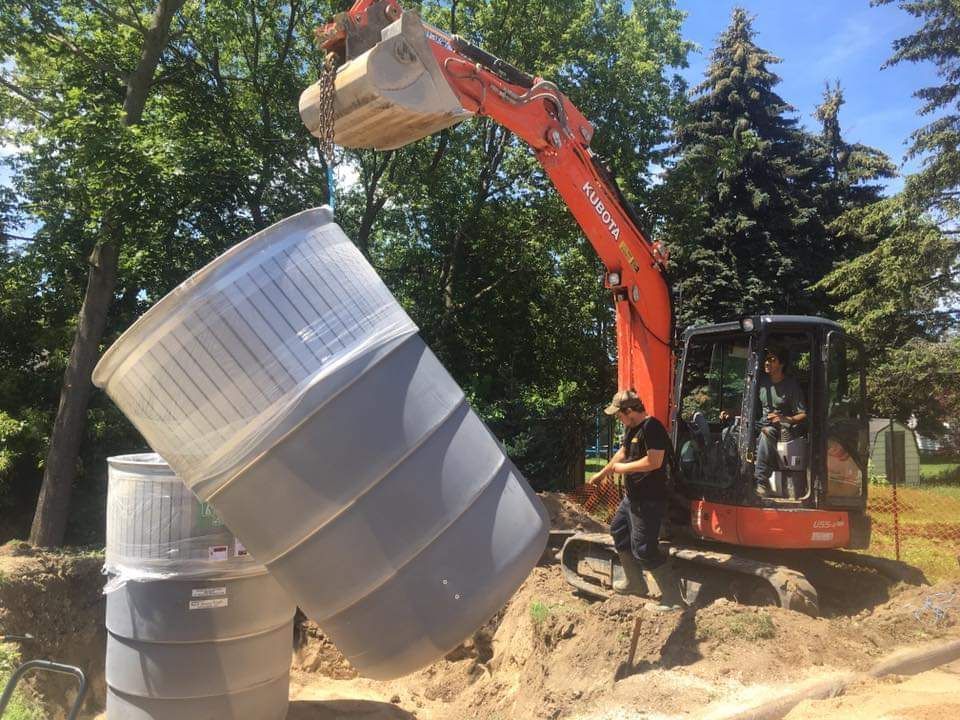 A man is loading a large plastic barrel into an excavator.