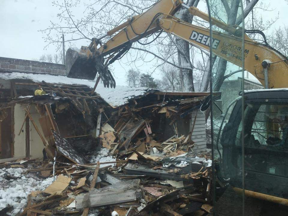 A deere excavator is demolishing a house in the snow