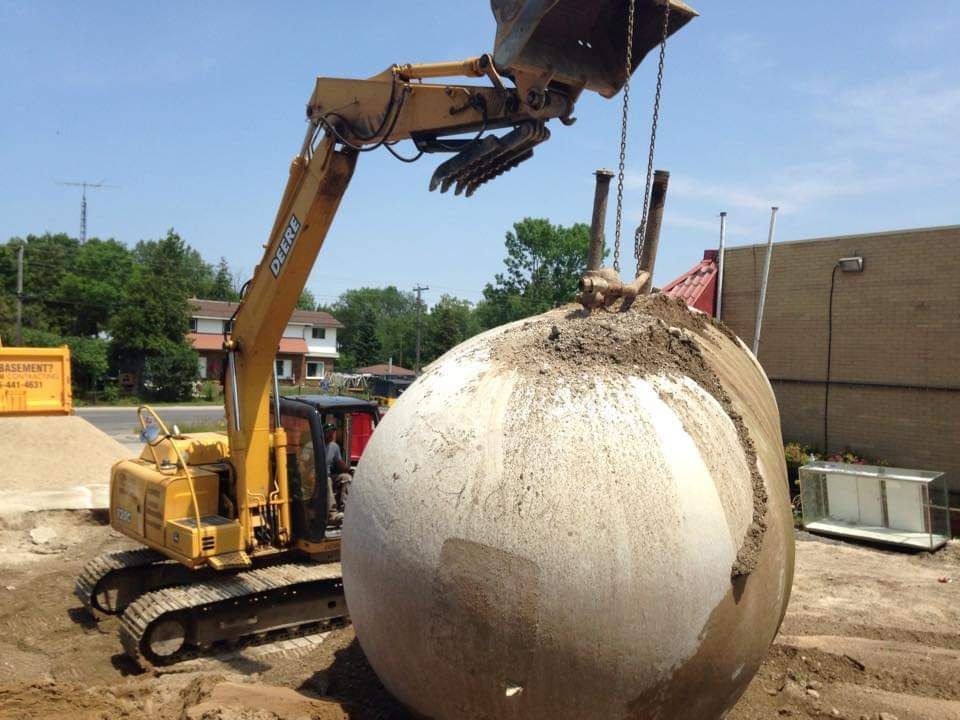 A large concrete ball is being lifted by a yellow excavator