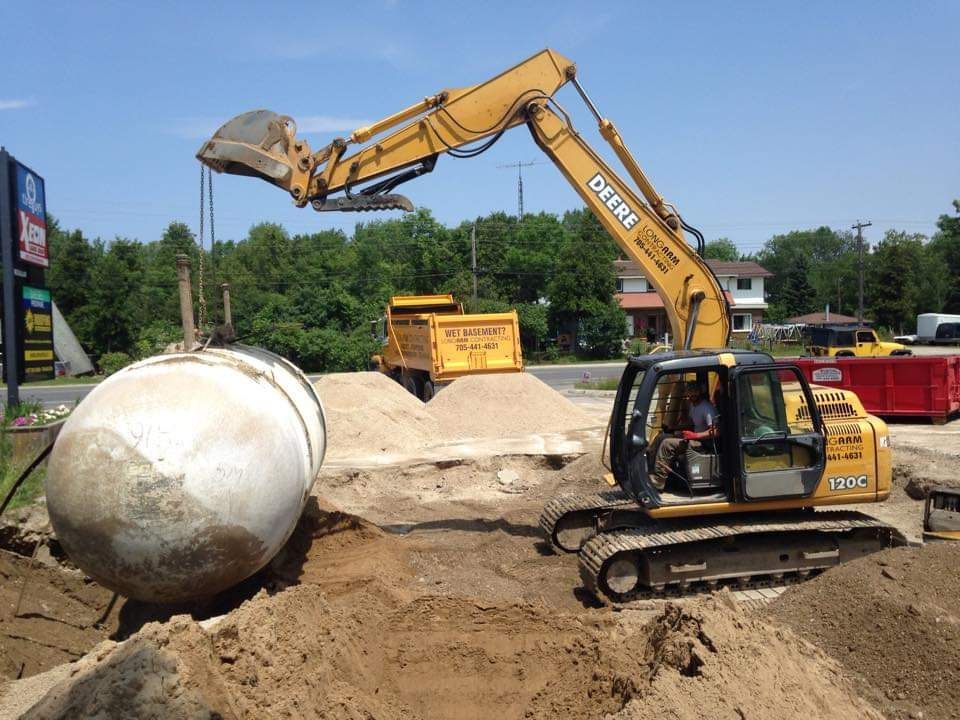 A large concrete cylinder is being lifted by a deere excavator