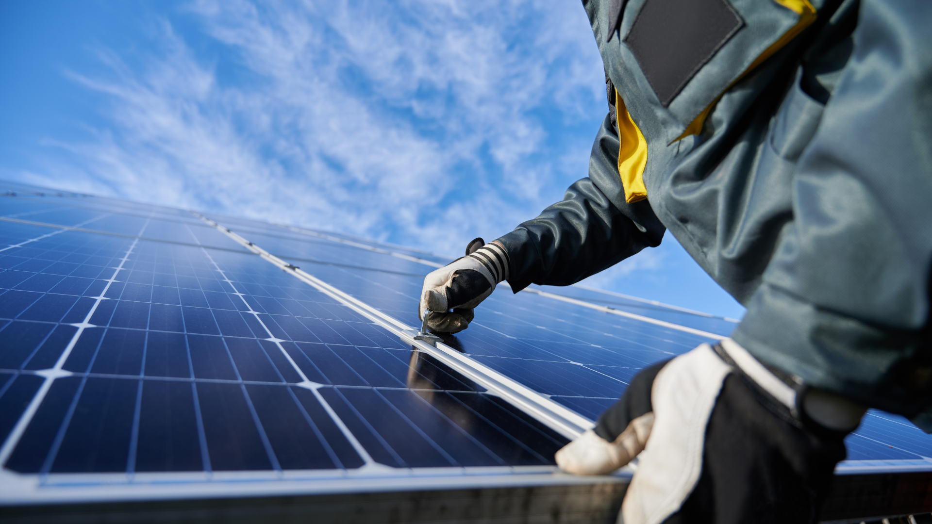 Person installing solar panels on a rooftop, blue sky in the background.