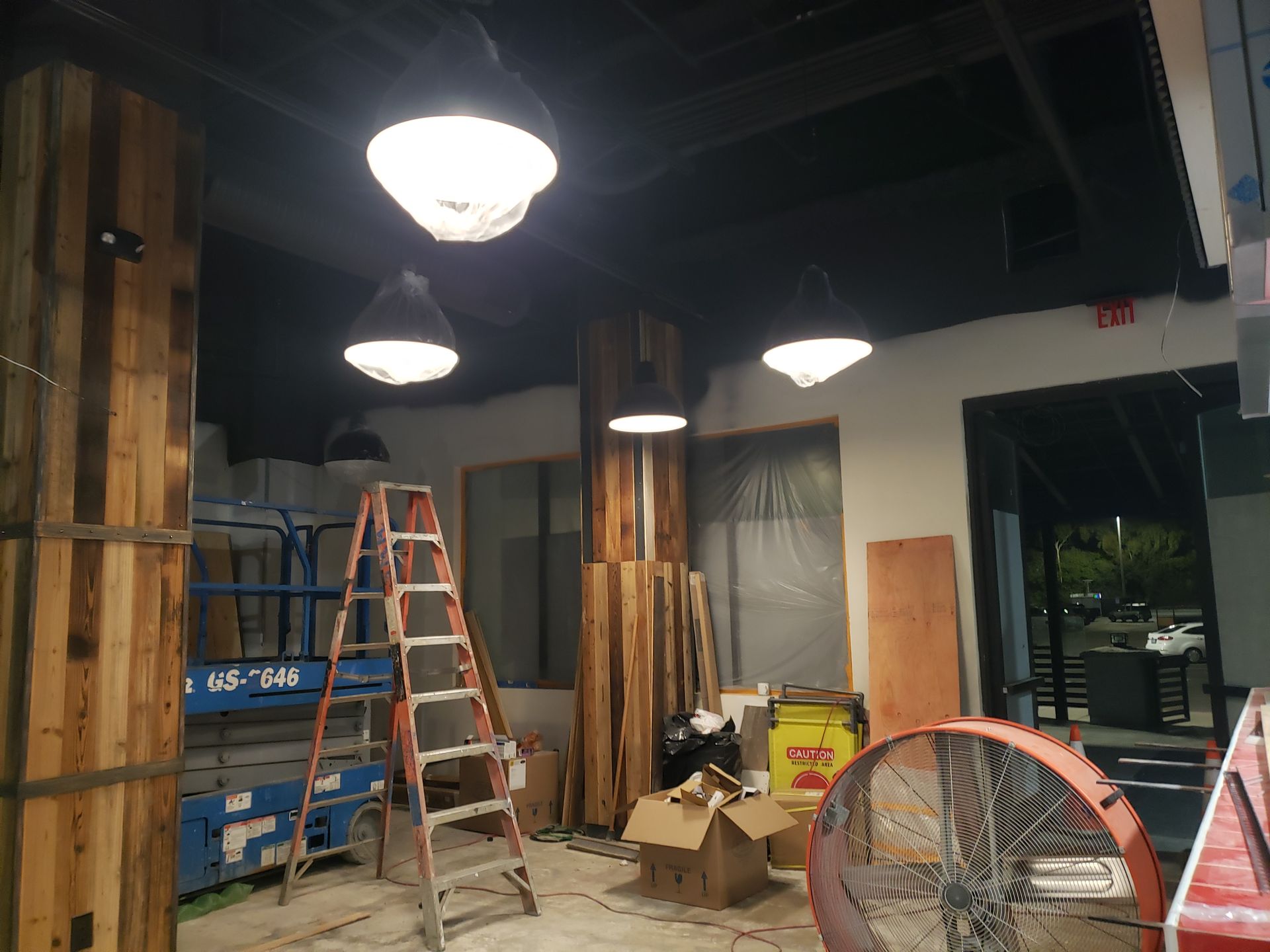 Interior construction: Workers, tools, and wood beams. Black ceiling, hanging lights.