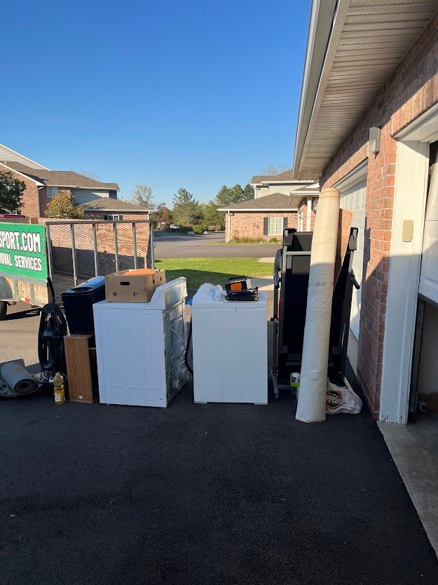 A collection of household items, including appliances, stacked outside a garage, ready for removal.
