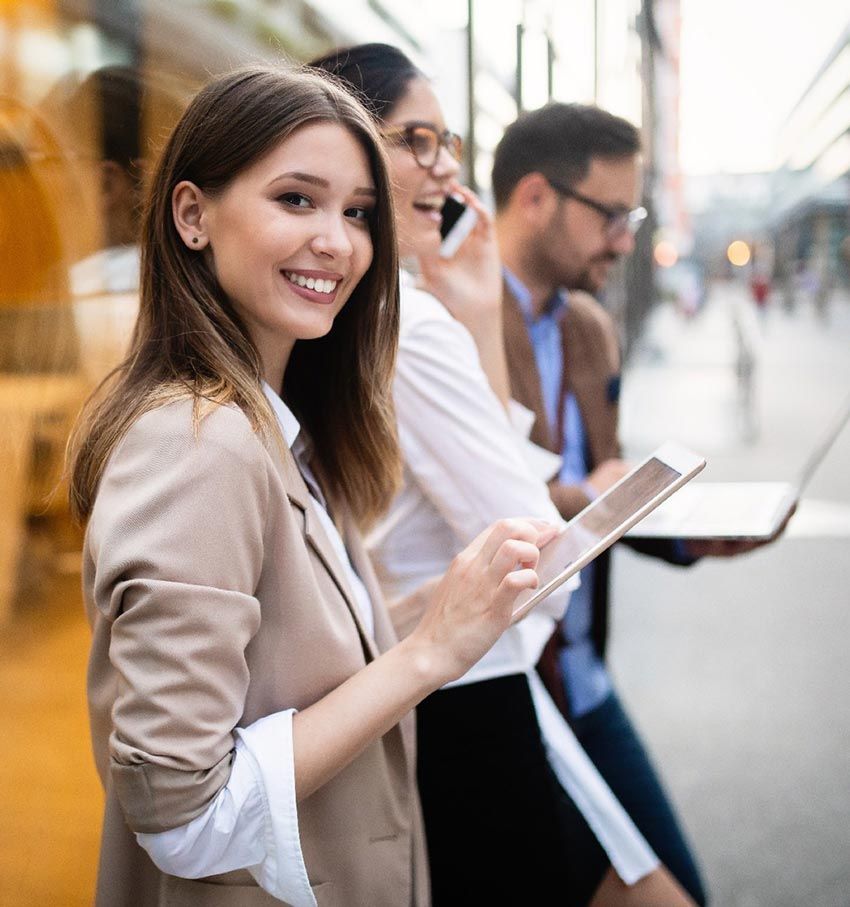 A woman is smiling while holding a tablet and talking on a cell phone.