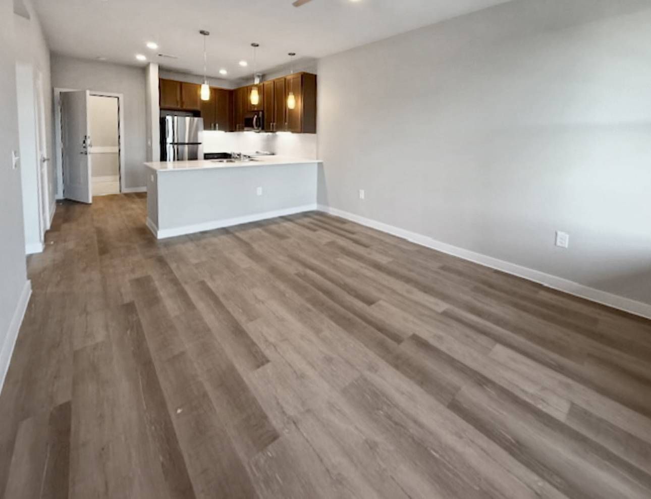 Open-concept living area with a kitchen island, stainless-steel appliances, and wood-look flooring.
