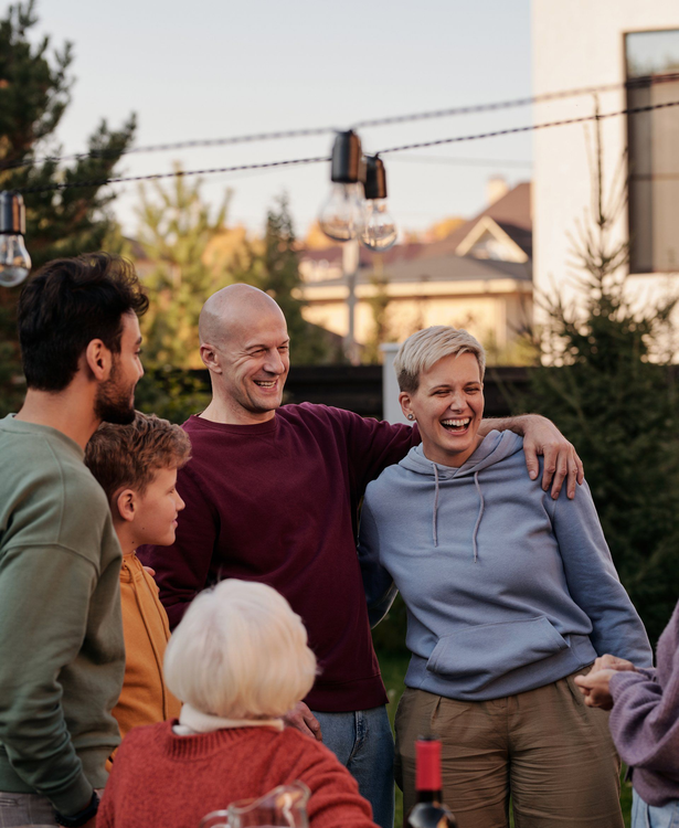 Family gathered outdoors laughing, embracing, with string lights overhead.
