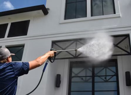Person power washing a white building's exterior.