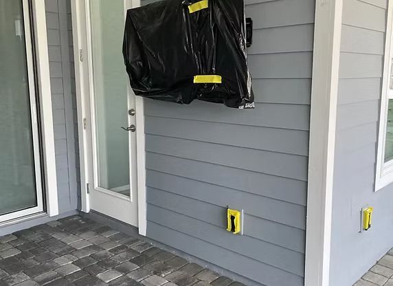 Black bag taped to a gray exterior wall. A door and an electrical outlet are also visible.
