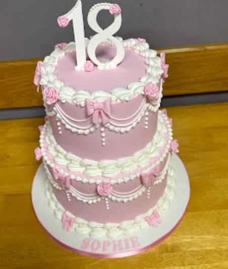 A pink and white, two-tier birthday cake. Butter cream around the outside with the colour fading from bright pink at the bottom to white at the top. Decorated with pink and white sugar butterflies.