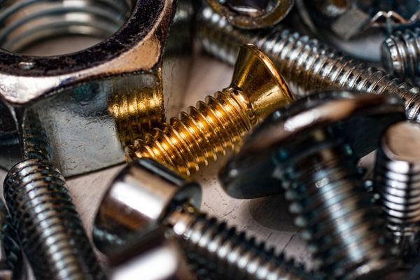 Primo piano di viti e bulloni metallici assortiti, tra cui una vite dorata tra elementi in metallo argentato.