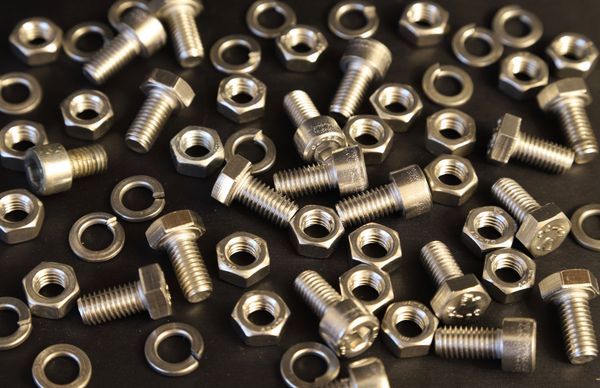 Dadi e bulloni esagonali argentati sparsi su una superficie scura