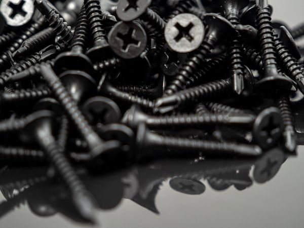 Un mucchio di viti nere con la testa argentata sparse su una superficie riflettente