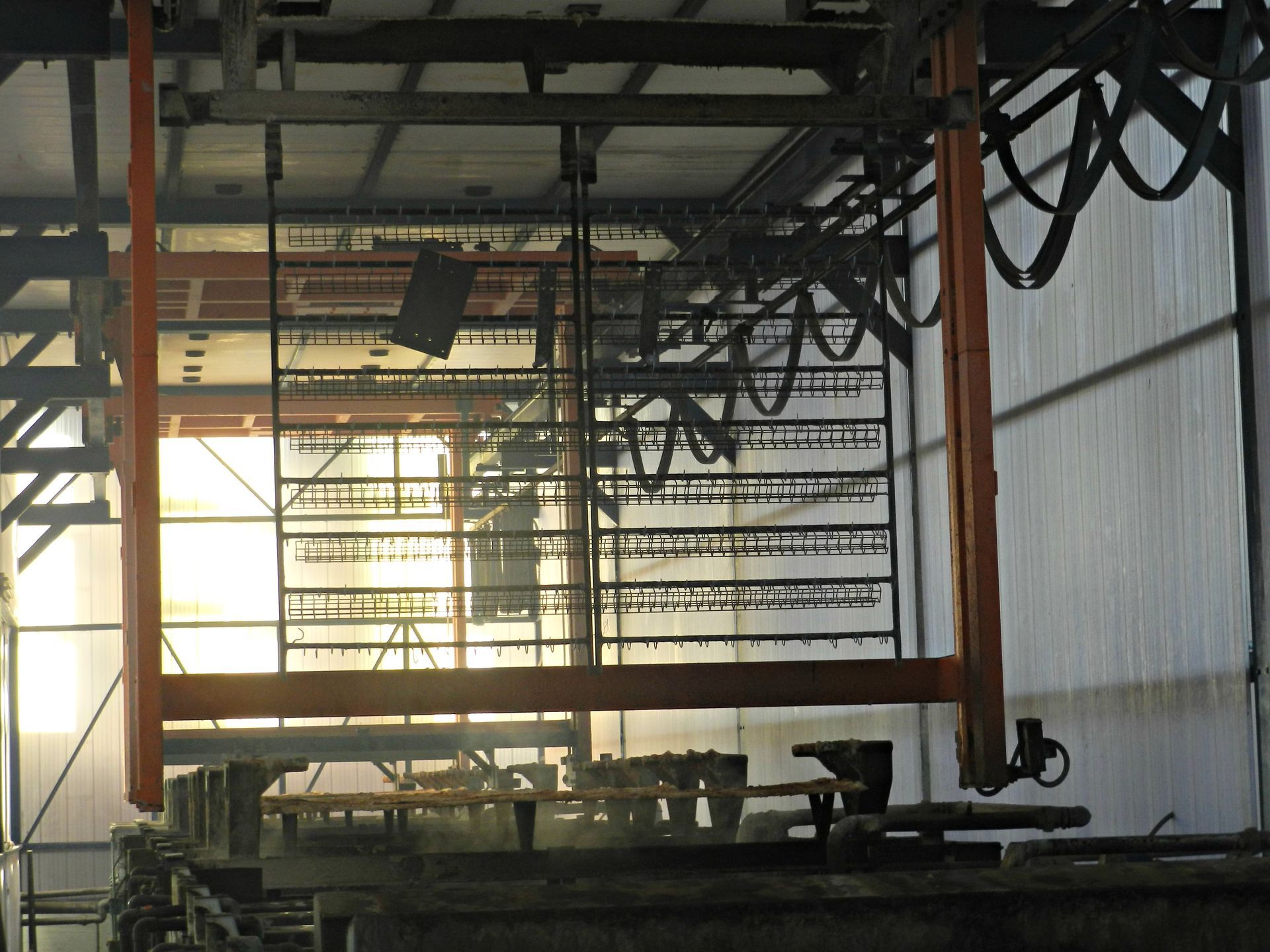 Interno industriale con impalcature metalliche, cavi sospesi e luce solare che filtra attraverso un'ampia finestra.