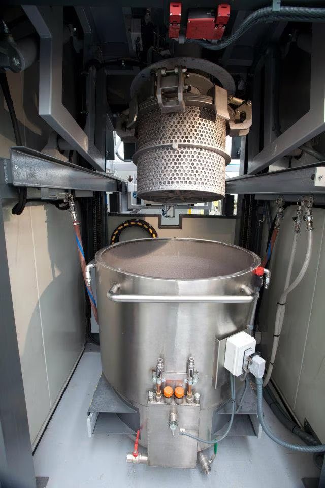 Macchina industriale con grande serbatoio in acciaio inox e tamburo a rete sospeso all'interno di un involucro metallico.