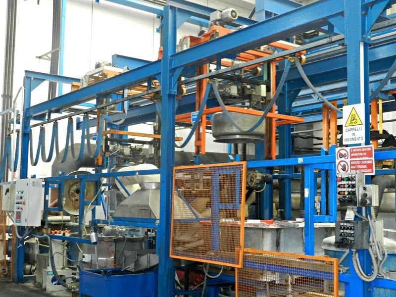 Macchinario industriale con telaio in acciaio blu, protezioni di sicurezza arancioni e tramogge metalliche in un'officina di fabbrica.