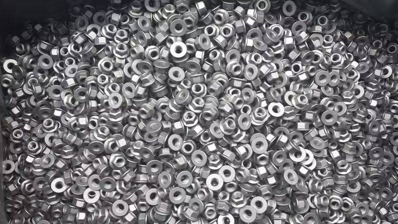 Un mucchio di piccole rondelle e occhielli metallici in scala di grigi, fittamente ammassati.