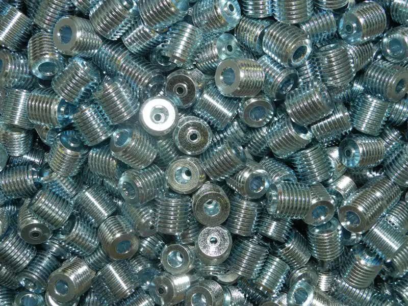 Un mucchio di inserti filettati in metallo lucido, sparsi ovunque.
