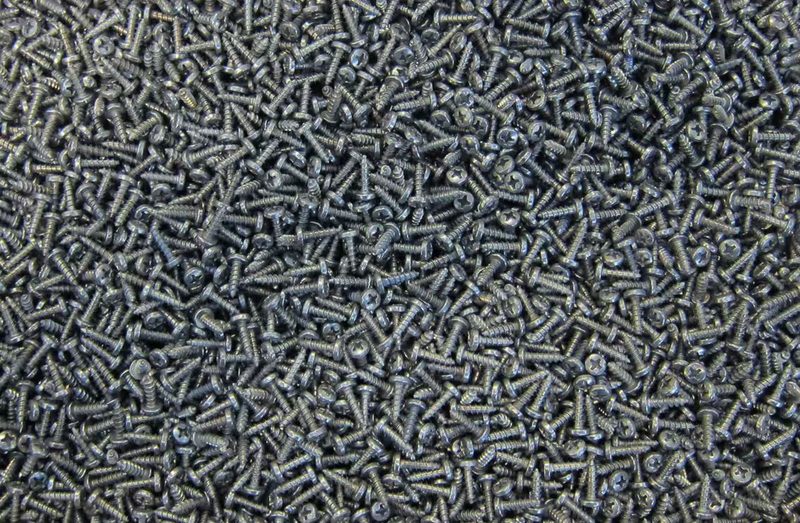 Primo piano di un mucchio di piccole viti o elementi di fissaggio in metallo grigio sparsi insieme