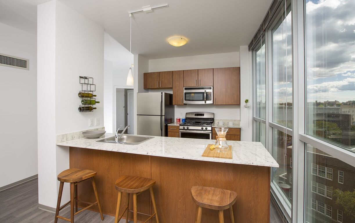 A kitchen with a large island , stools , a refrigerator and a microwave at  LMP Apartments in MO.