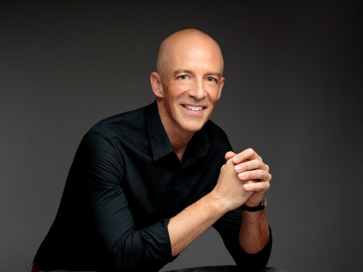 Man in a black shirt smiling with his hands folded.