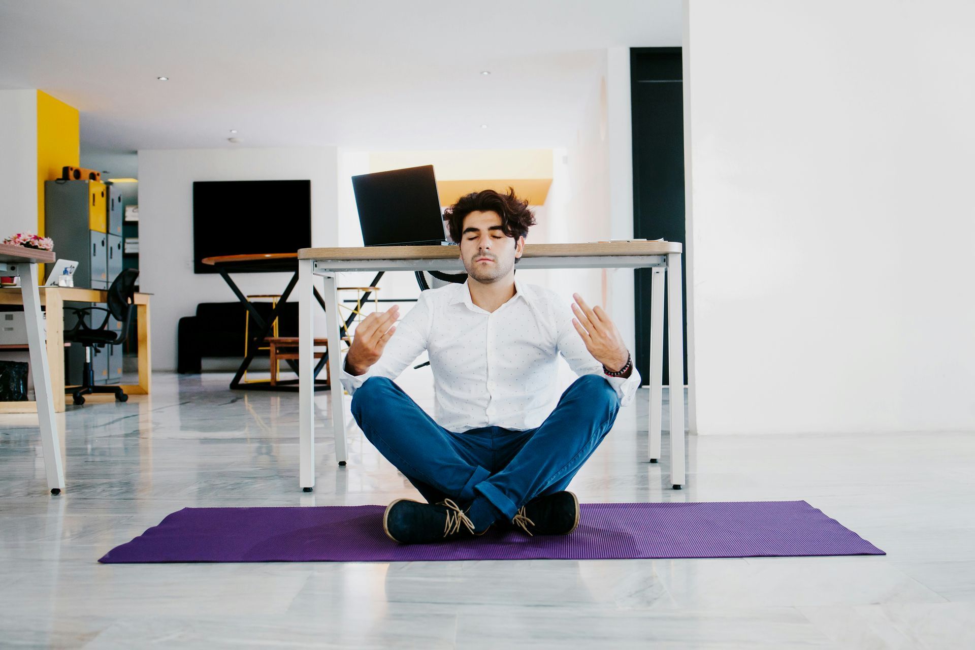 A young entrepreneur is relaxing and sitting on a yoga mat in an office.