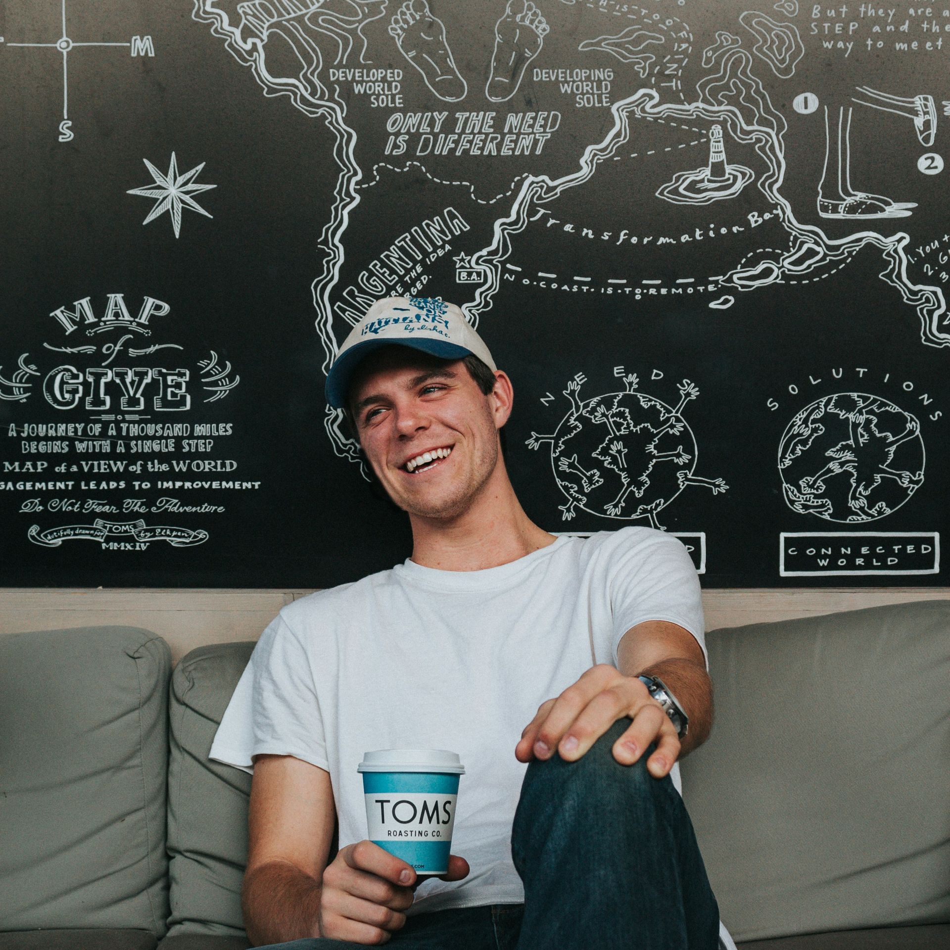 A man sitting on a couch holding a cup of toms coffee