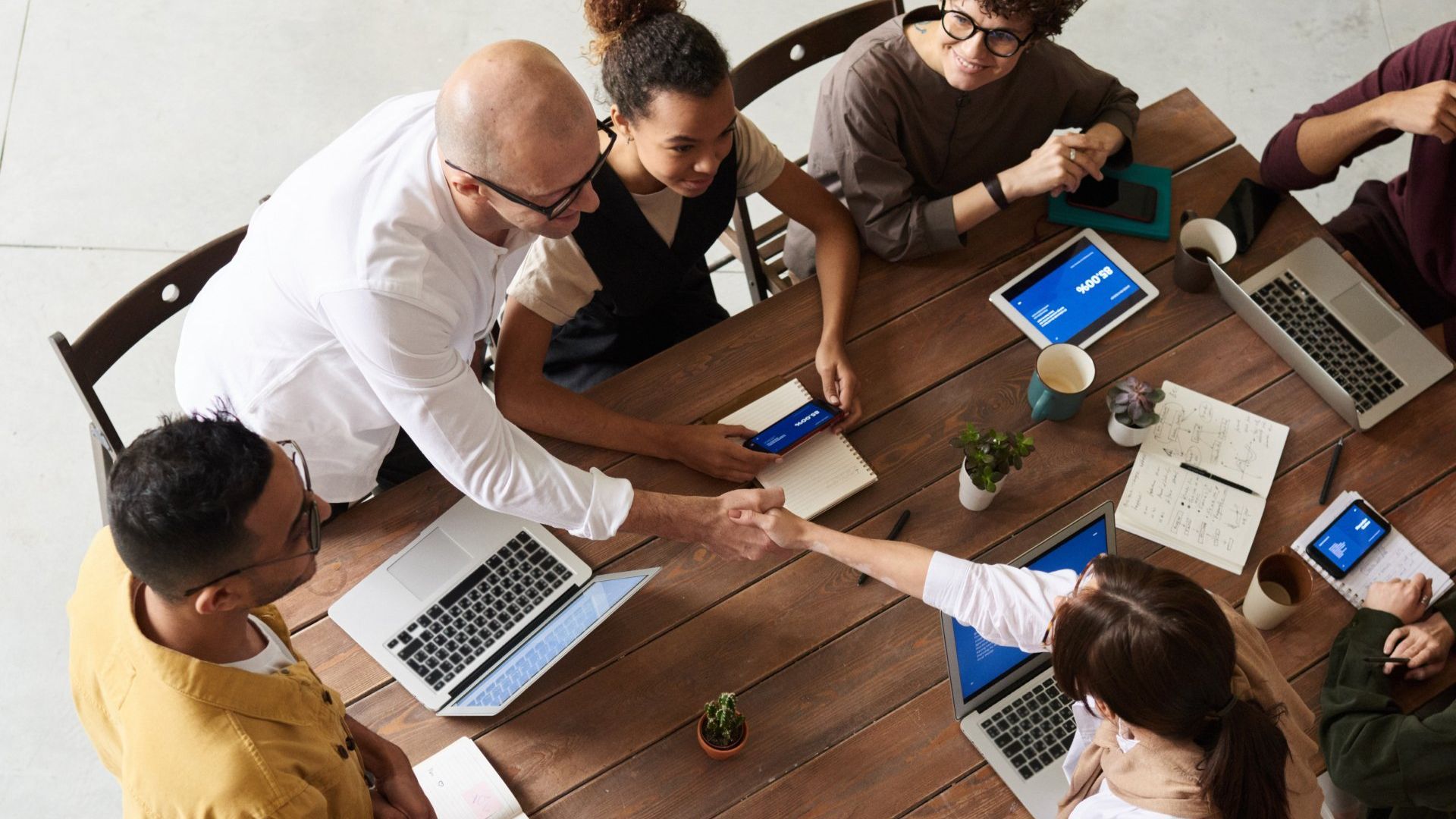 A group of entrepreneurs are sitting around a table shaking hands.