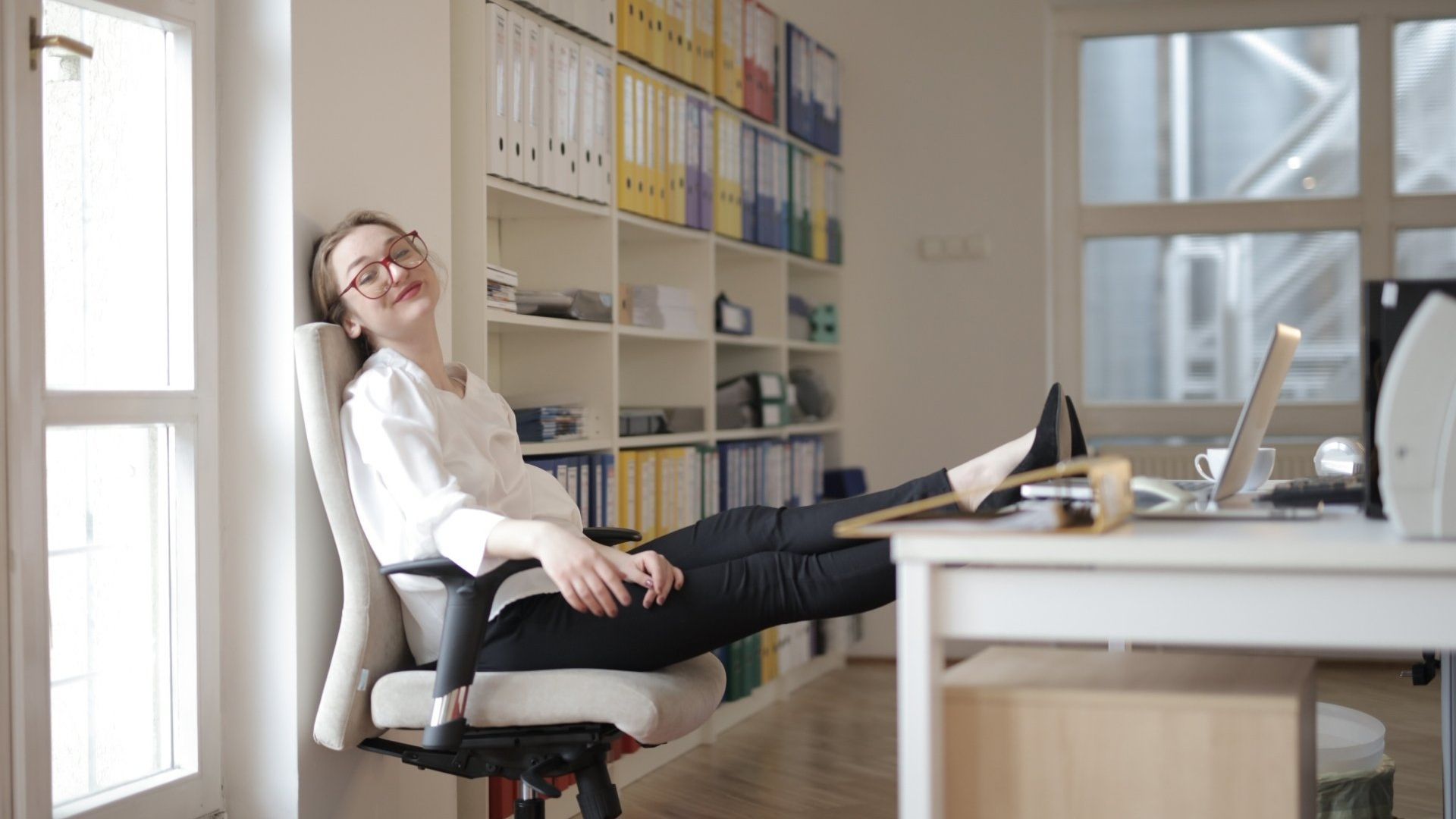 A woman is sitting in an office chair relaxing with her feet up on a desk.