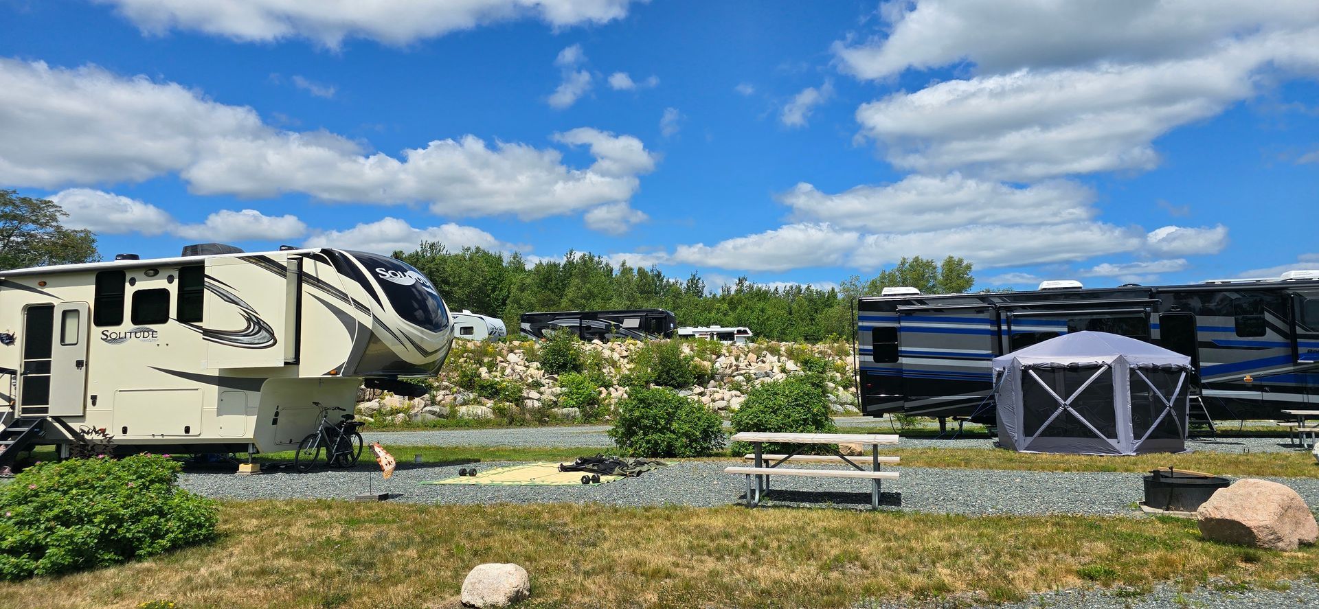 Campground with RVs, trees, picnic table, and blue sky with clouds.