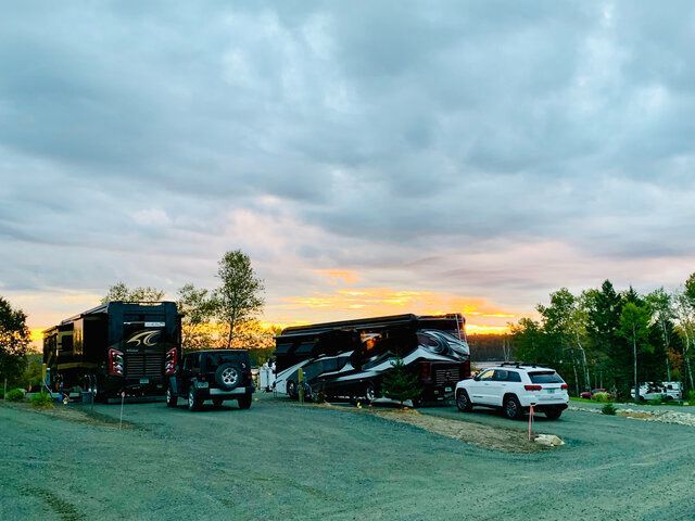 Two RVs and two SUVs parked at a campsite during sunset, with a cloudy sky and orange and yellow hues.