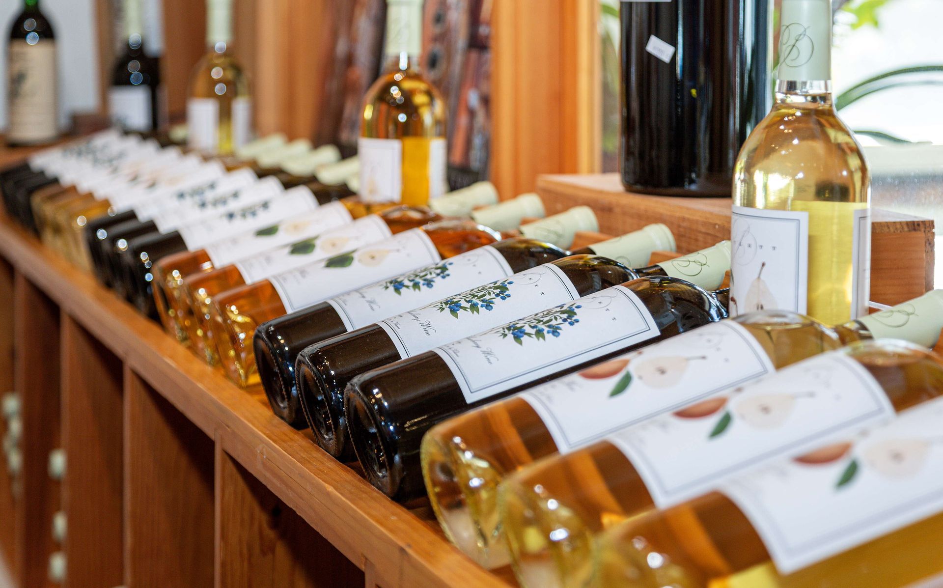 Bottles of wine in various colors arranged on wooden shelves in a store setting.