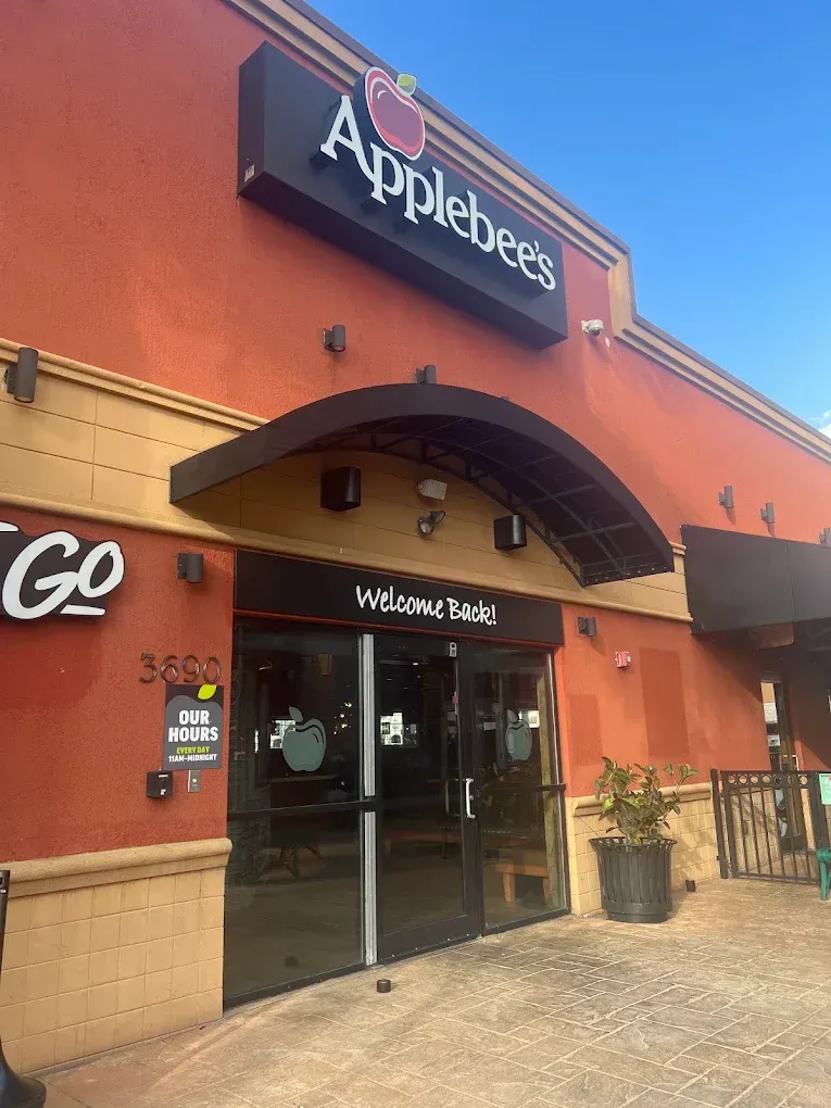A large crowd sits in an outdoor amphitheater at dusk, watching a performance on a lighted, arched stage framed by trees.