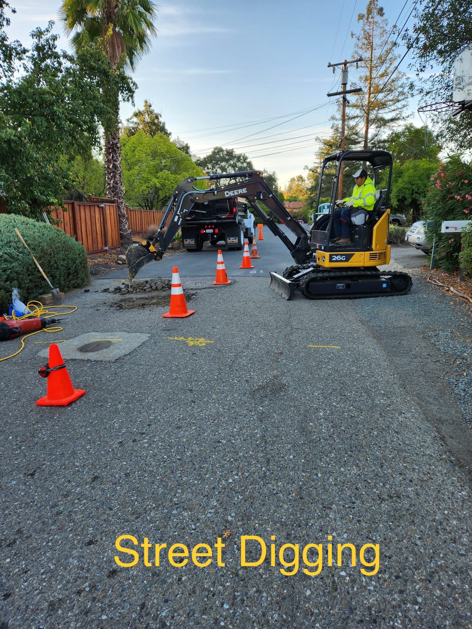 A yellow excavator is digging a hole in the street.