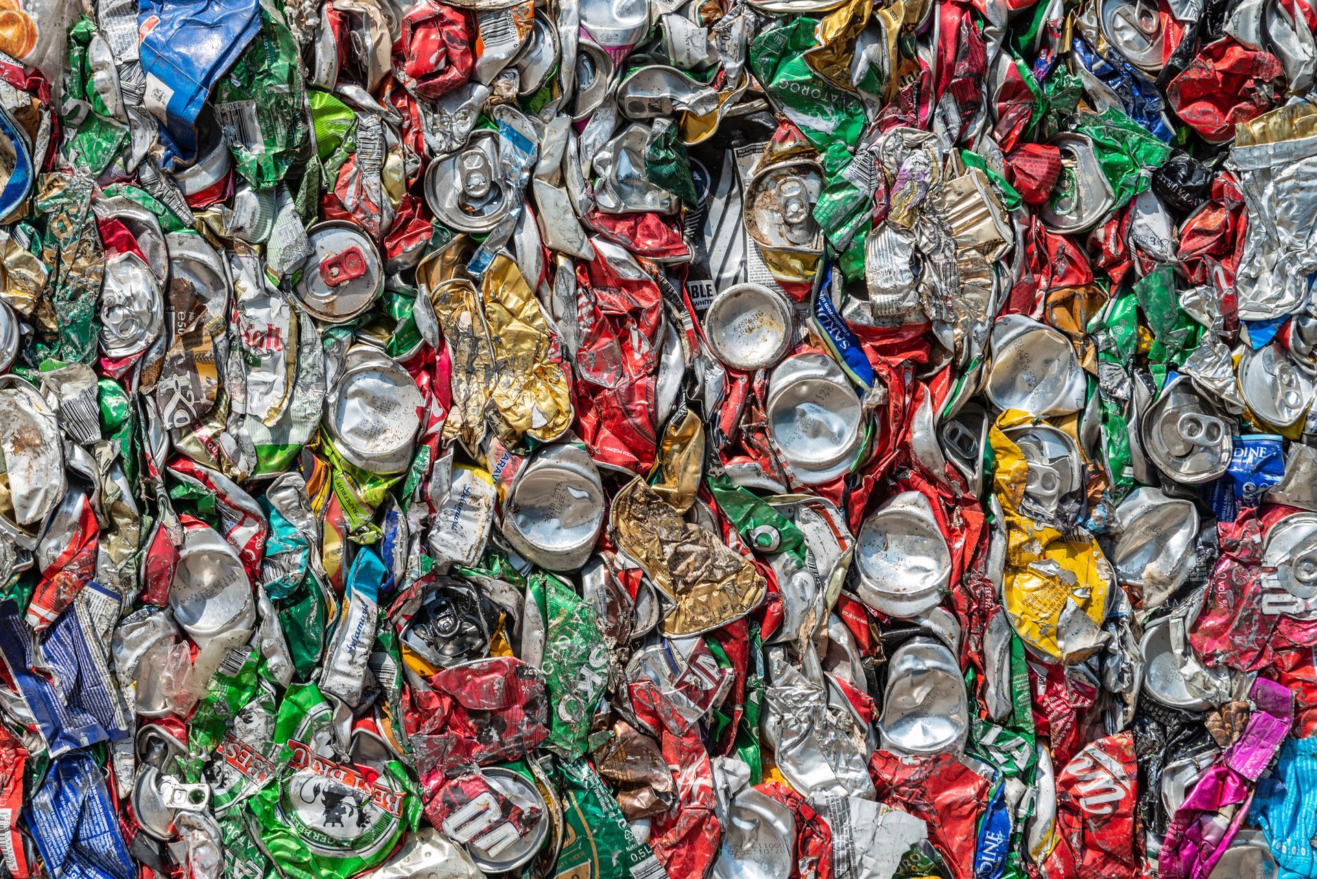 Tightly packed crushed aluminum cans in various colors at a recycling center.