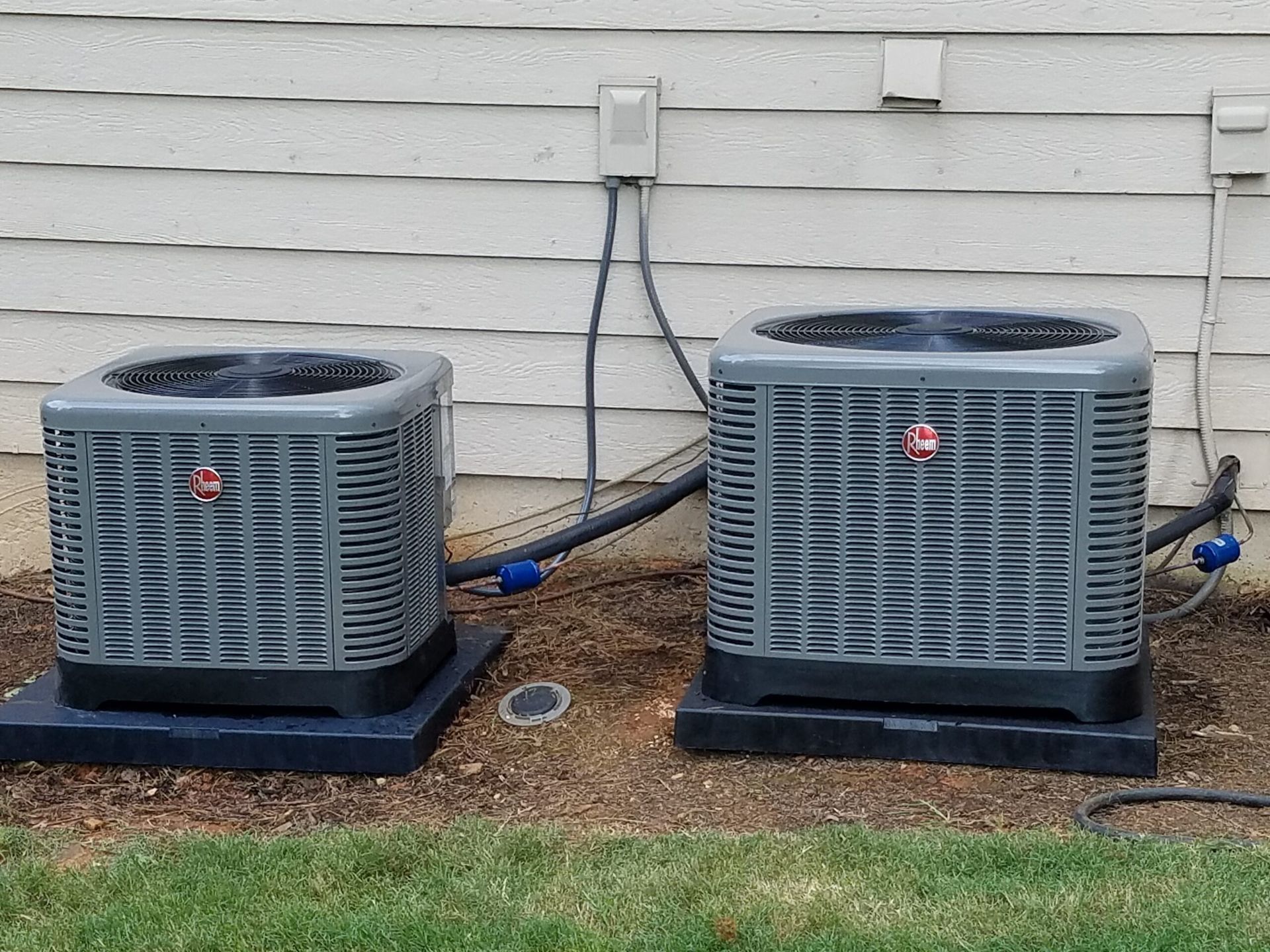 Two air conditioners are sitting next to each other outside of a house