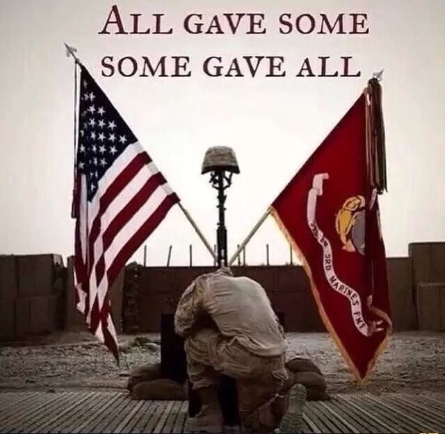 A soldier kneeling in front of two flags with the words all gave some some gave all