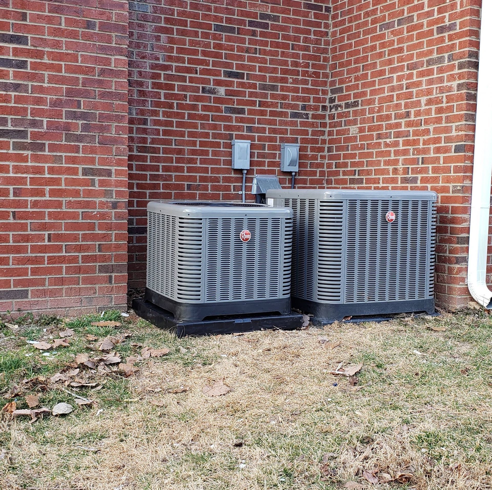 Two air conditioners are sitting in front of a brick wall
