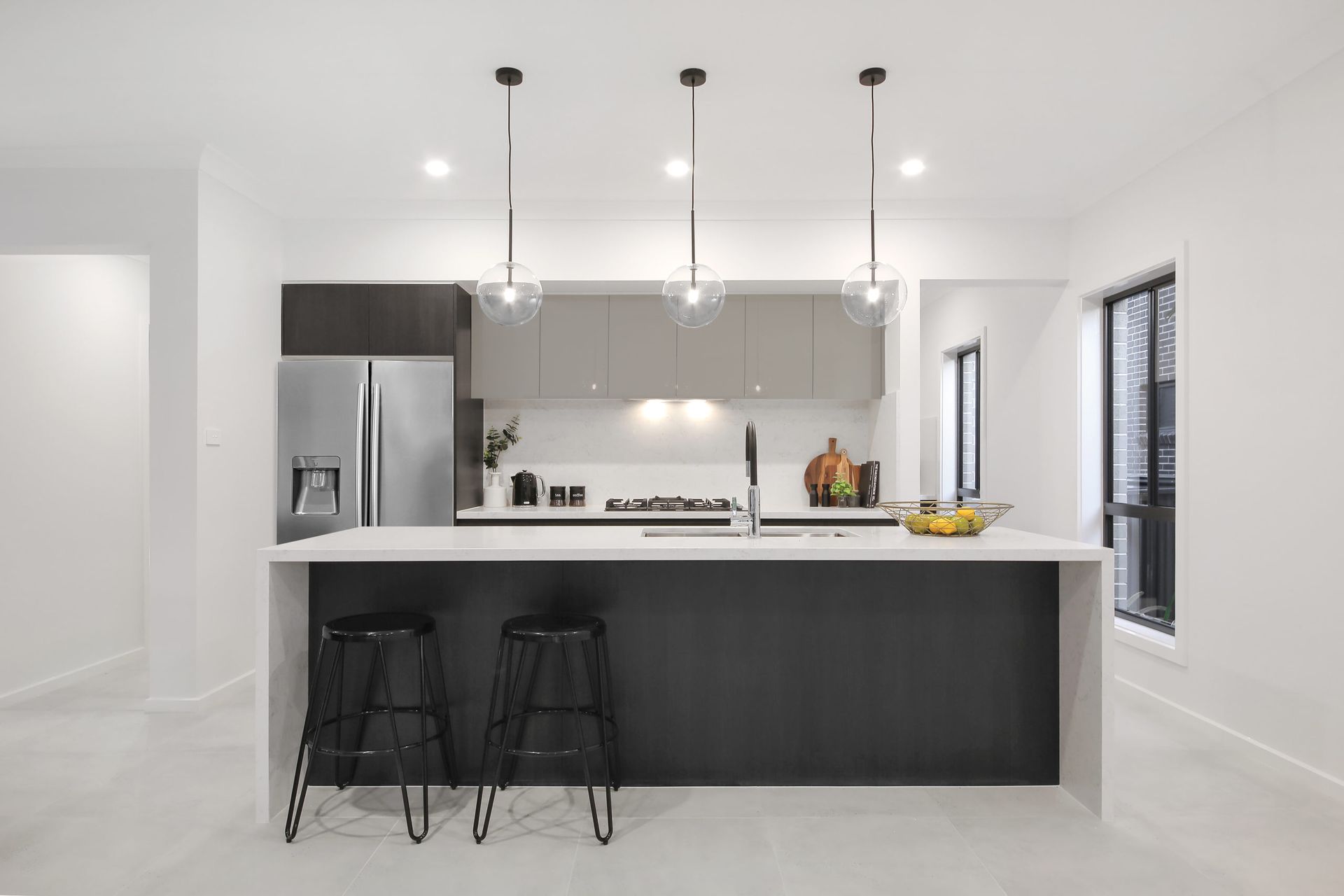 Sanctuary 37 home design - A minimalist kitchen with a large island, stools and a refrigerator.
