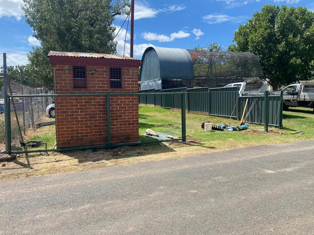 A Brick Building Is Sitting Next to A Fence on The Side of The Road — DW Fencing Tamworth in Taminda, NSW