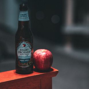 a bottle of angry orchard hard cider next to an apple