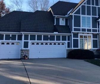 A large house with a black roof and white garage doors